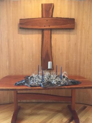 The wooden altar table holds four dark blue tapers surrounding a large white pillar candle on a dark velvelt cloth with an unruly bundle of starry wire serving as the Advent "wreath"